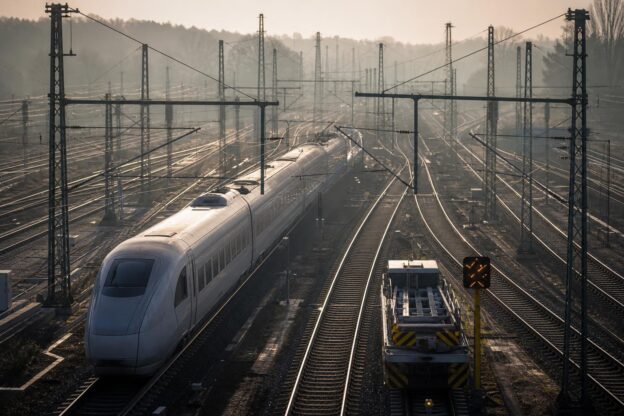 Ein Hochgeschwindigkeitszug fährt durch einen Bahnknoten mit mehreren parallel verlaufenden Gleisen und Oberleitungen in